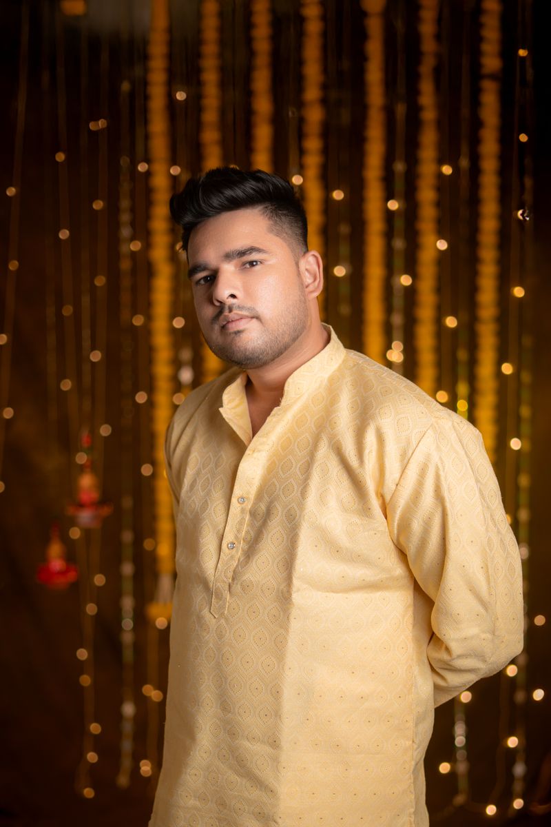 Man in traditional yellow kurta with festive background lighting.